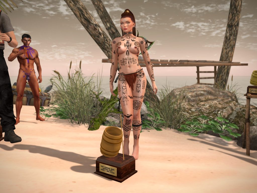 A beautiful topless woman with intricate body paint stands by a trophy on a sandy beach, with a bare man in the background