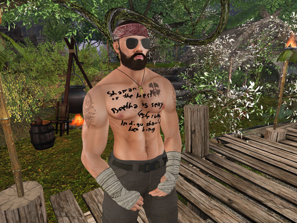 Shirtless villager stands on wooden platform in a jungle camp with trees and fire nearby