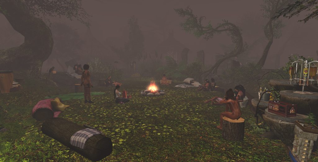 A group sits around a fire in a jungle camp, surrounded by mist and trees